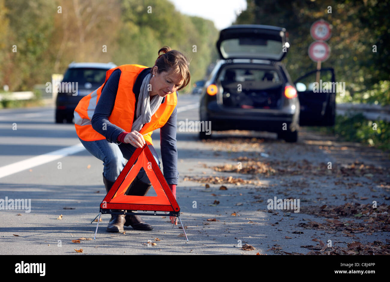 Ripartizione per auto, su una autostrada, driver femminile, indossa una divisa da lavoro ad alta visibilità, impostare un triangolo di avvertenza. Foto Stock