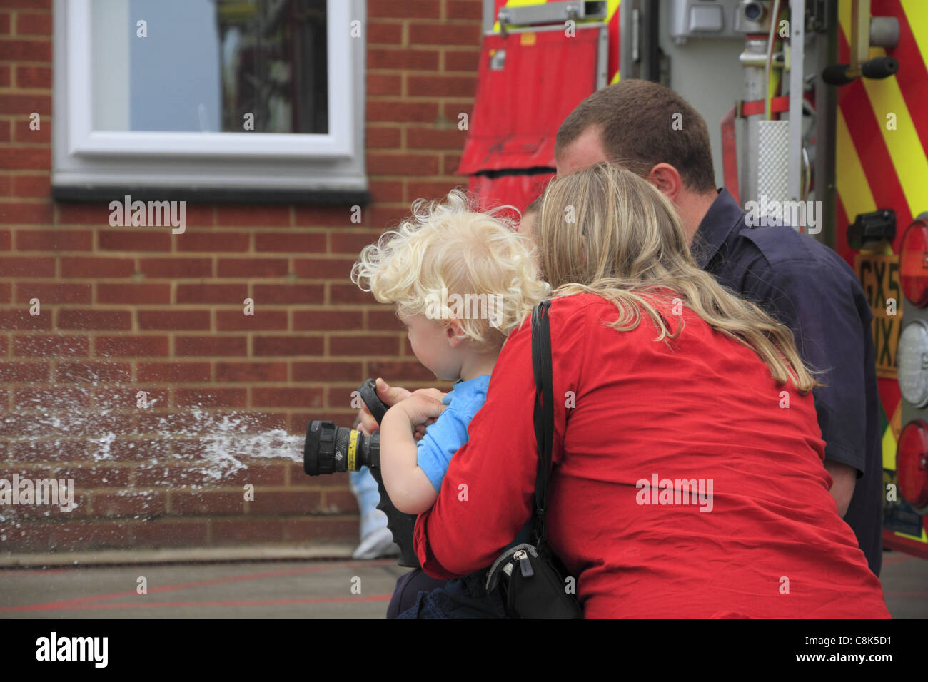 Una madre e suo figlio toddler utilizzare la manichetta antincendio in corrispondenza di una stazione di fuoco visita a Eastbourne, East Sussex, Inghilterra. Foto Stock