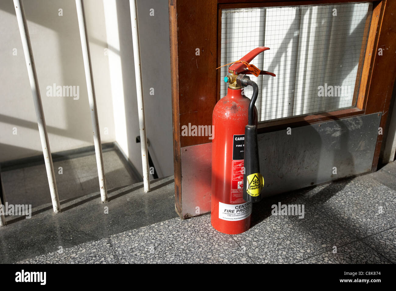 Estintore tenendo un incendio porta aperta nella parte superiore di un gruppo di scale in una vecchia fabbrica di unità di magazzino Foto Stock