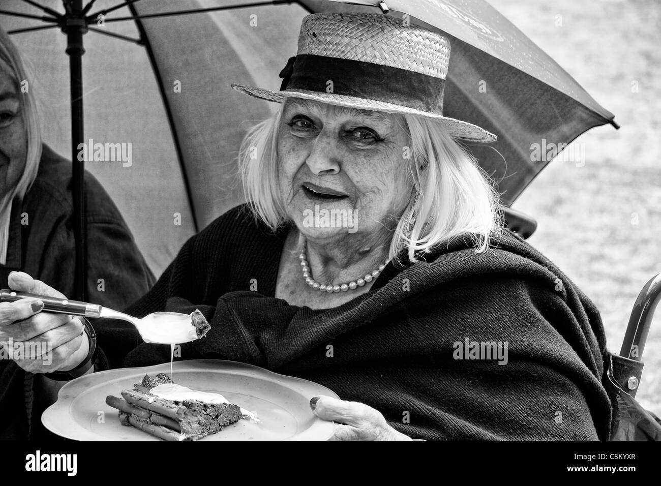 Donna anziana che indossa un diportista più paglia di mangiare una torta al cioccolato Foto Stock