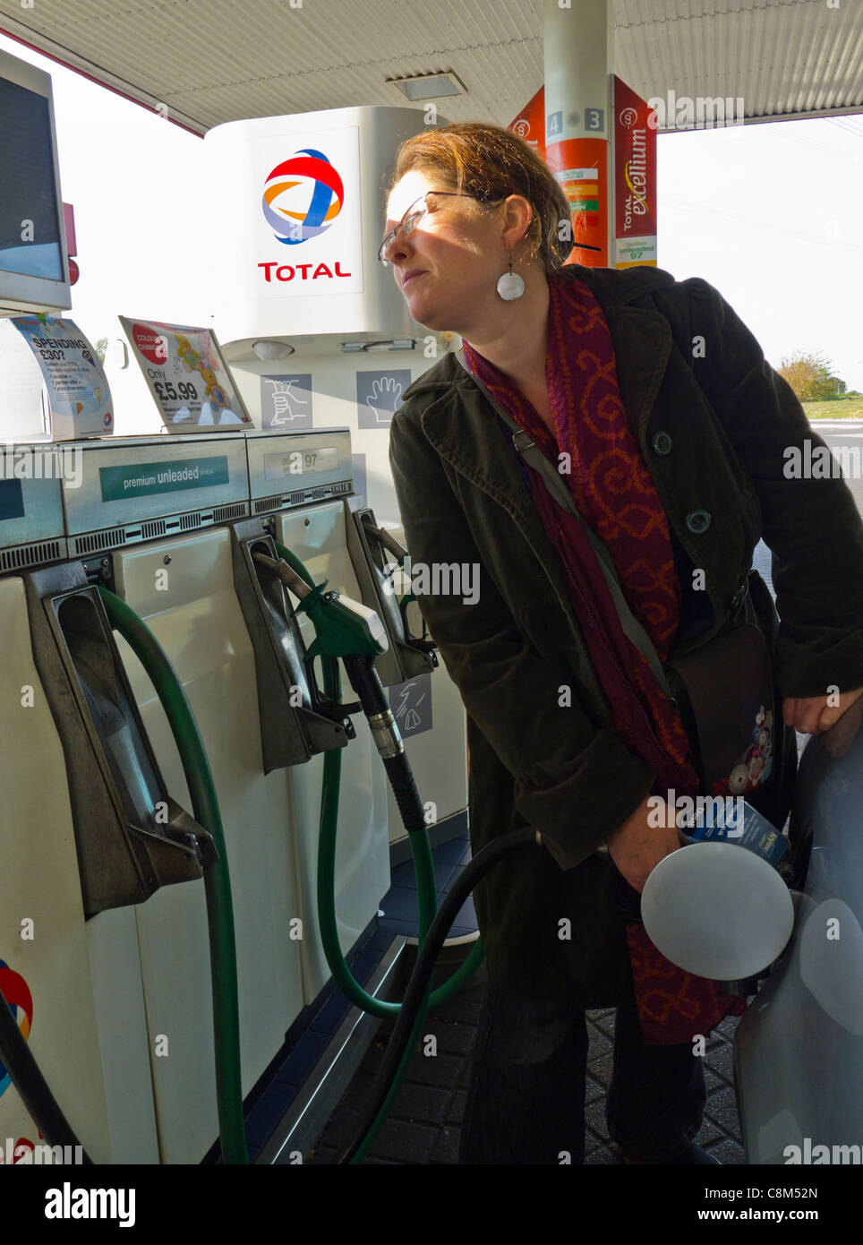 Una donna si riempie la sua vettura con il carburante mentre si guarda il prezzo. Foto Stock