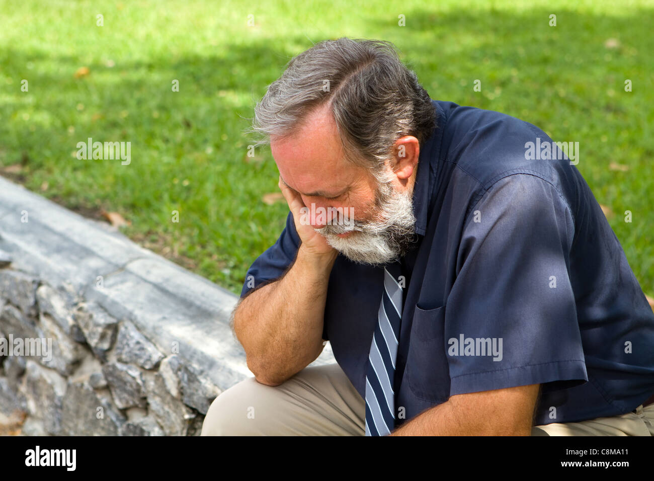 Imprenditore premuto dalle condizioni economiche si siede malinconico in un parco con la sua testa in mano. Foto Stock
