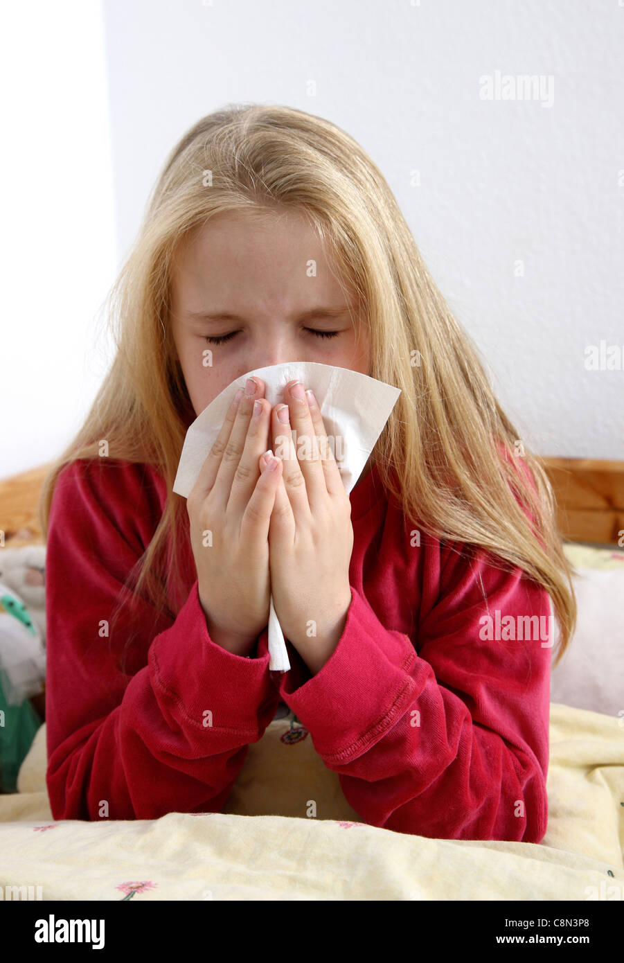 Ragazza giovane, 10 anni, giace ammalata a letto, a casa con un influenza, starnuti. Foto Stock