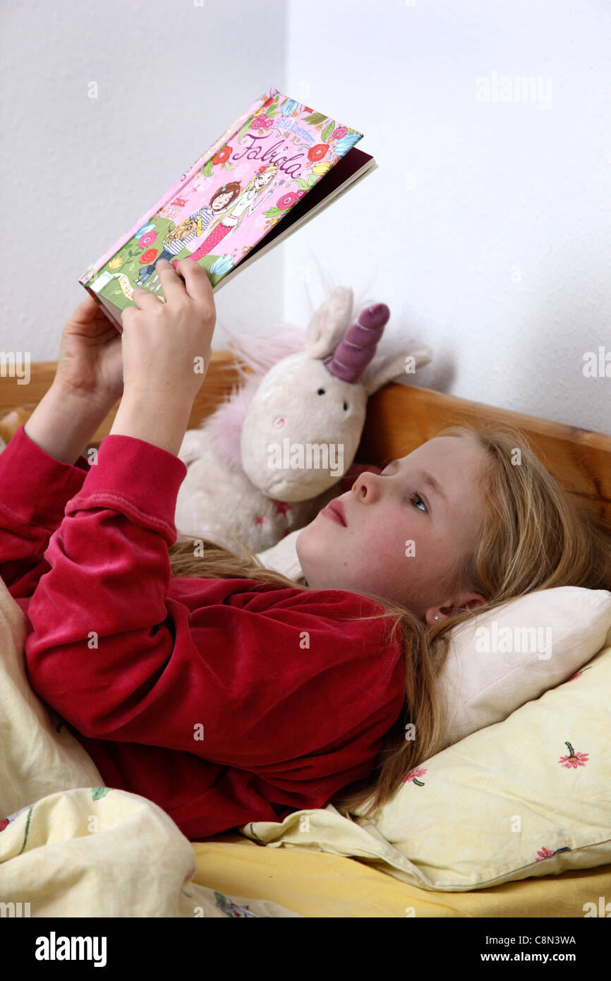 Ragazza giovane, 10 anni, la lettura di un libro nel suo letto. Foto Stock