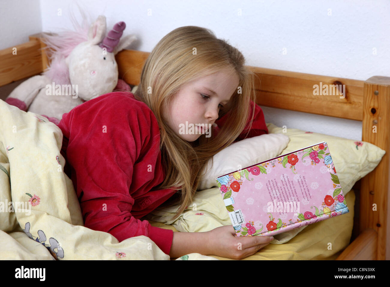 Ragazza giovane, 10 anni, la lettura di un libro nel suo letto. Foto Stock