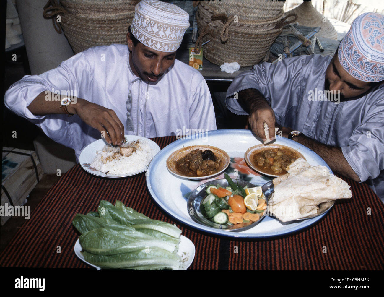 Due uomini musulmani mangiano usando solo la mano destra per selezionare porzioni di cibo, Oman Foto Stock