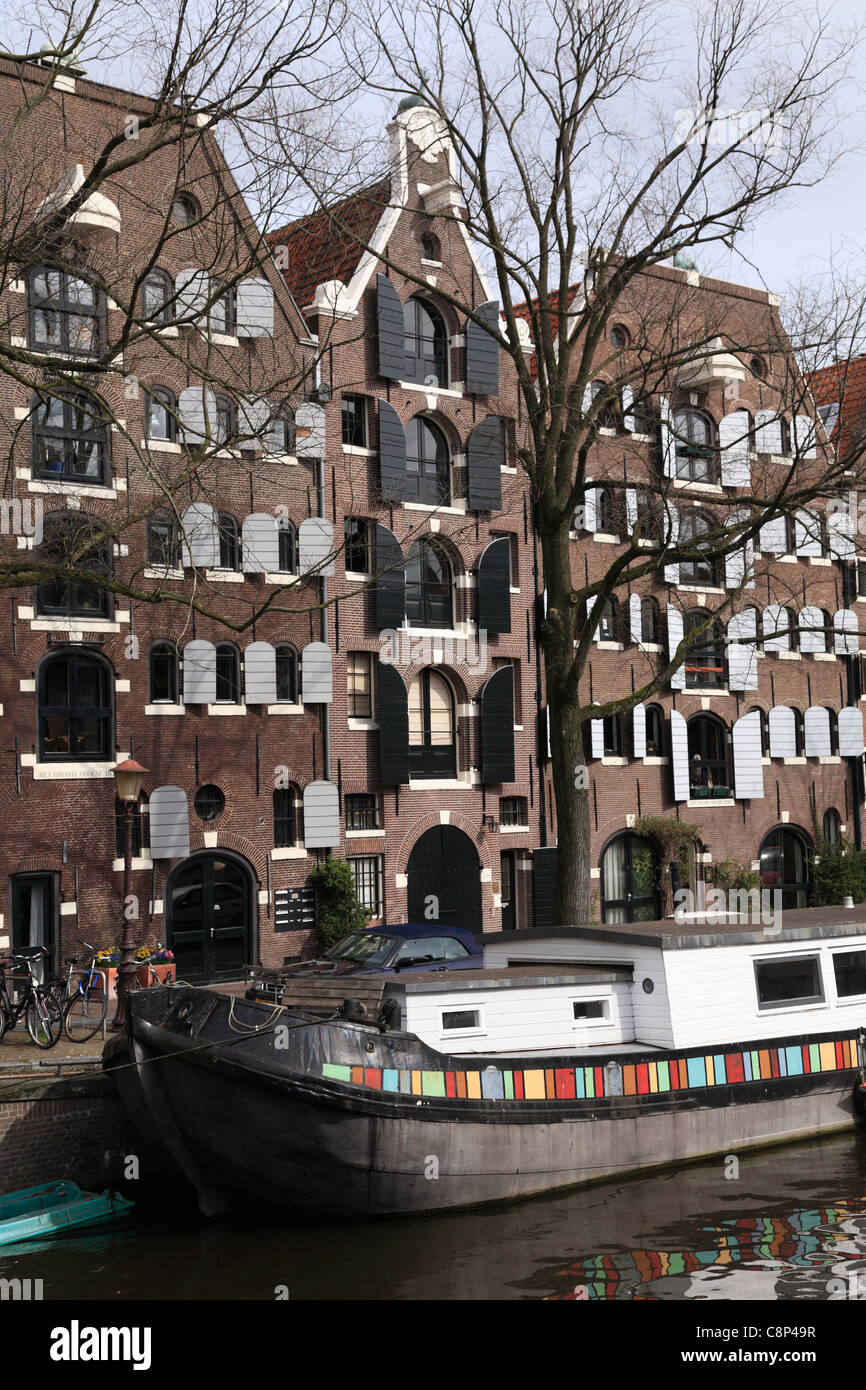 Casa galleggiante olandese barge e vecchi magazzini case su un canale nel quartiere Jordaan di Amsterdam Holland Olanda in primavera Foto Stock