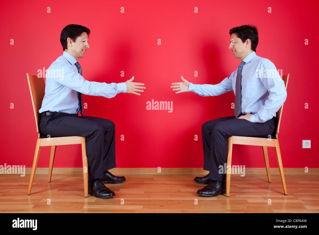 Accordo di stretta di mano tra due letti imprenditore seduto in una sedia accanto ad una parete rossa Foto Stock