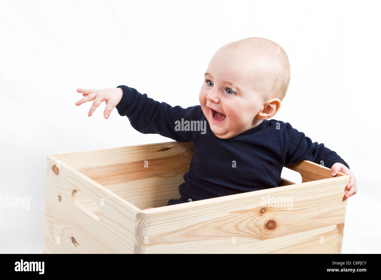 Un giovane bambino seduto in una scatola di legno rivolta verso sinistra Foto Stock