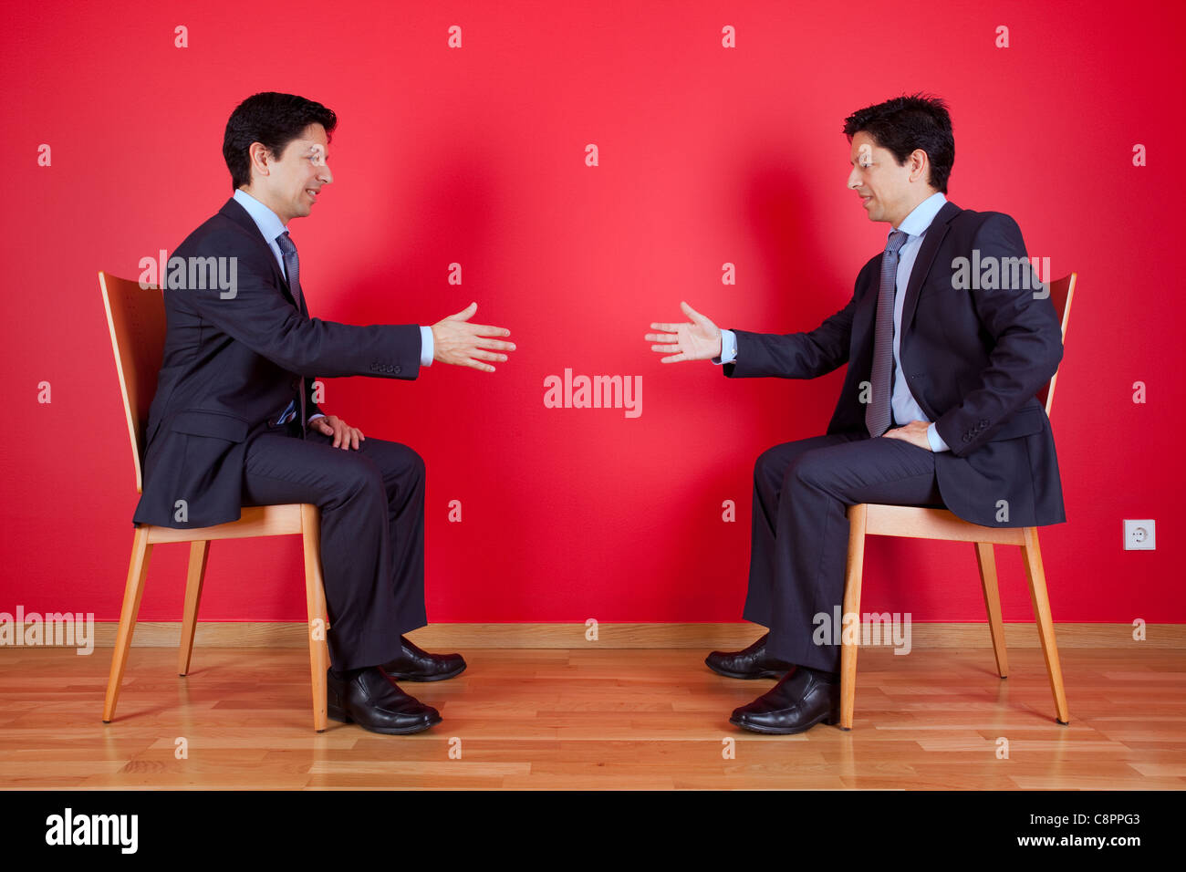 Accordo di stretta di mano tra due letti imprenditore seduto in una sedia accanto ad una parete rossa Foto Stock