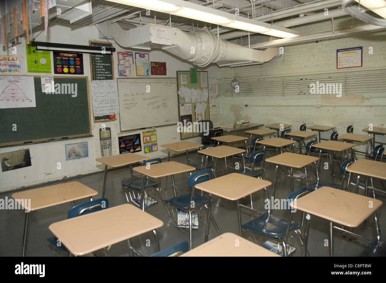 Pubblico scuola di alta classe sovraffollati con scrivanie, peeling vernice, senza finestre e un esposto ventilatore industriale per la ventilazione. NY Foto Stock