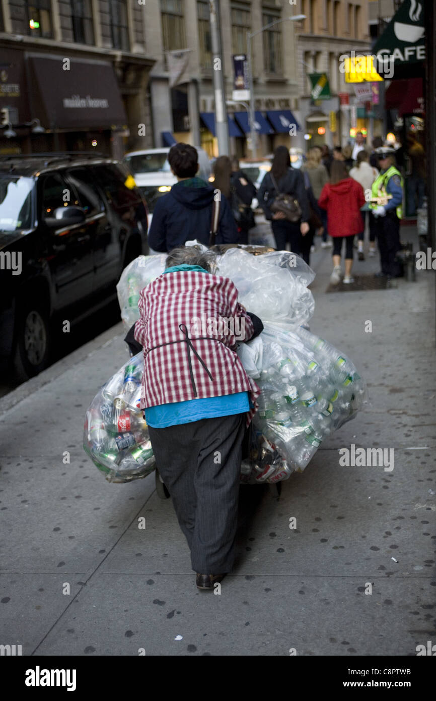 Donna anziana la raccolta di lattine in alluminio sulla strada a New York del quartiere finanziario riflette economia statunitense e la povertà crescente Foto Stock