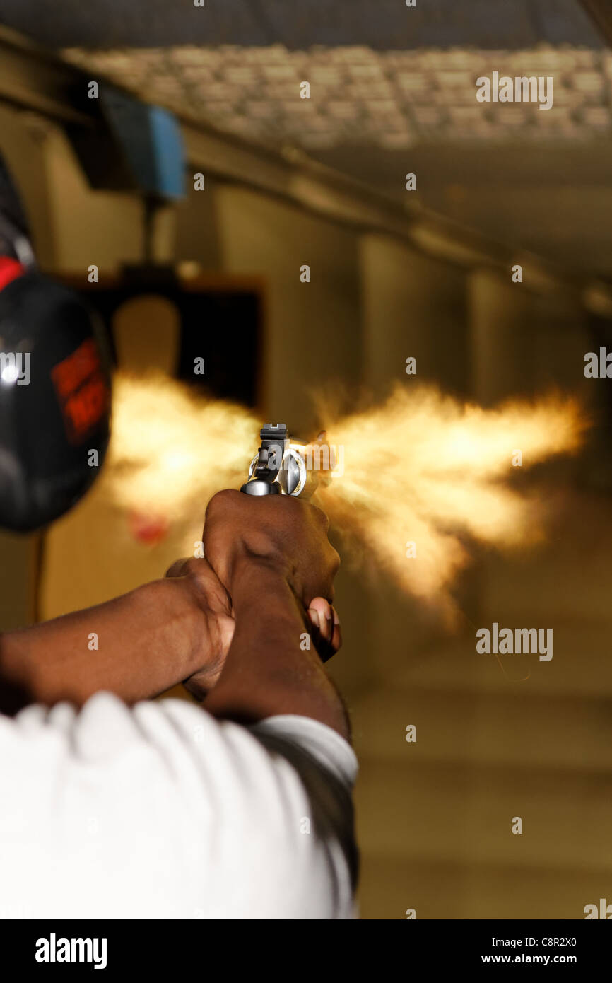 Foto scattate sopra la spalla di un giovane uomo di sparare una pistola a un poligono di tiro nel momento preciso del muso flash. Foto Stock
