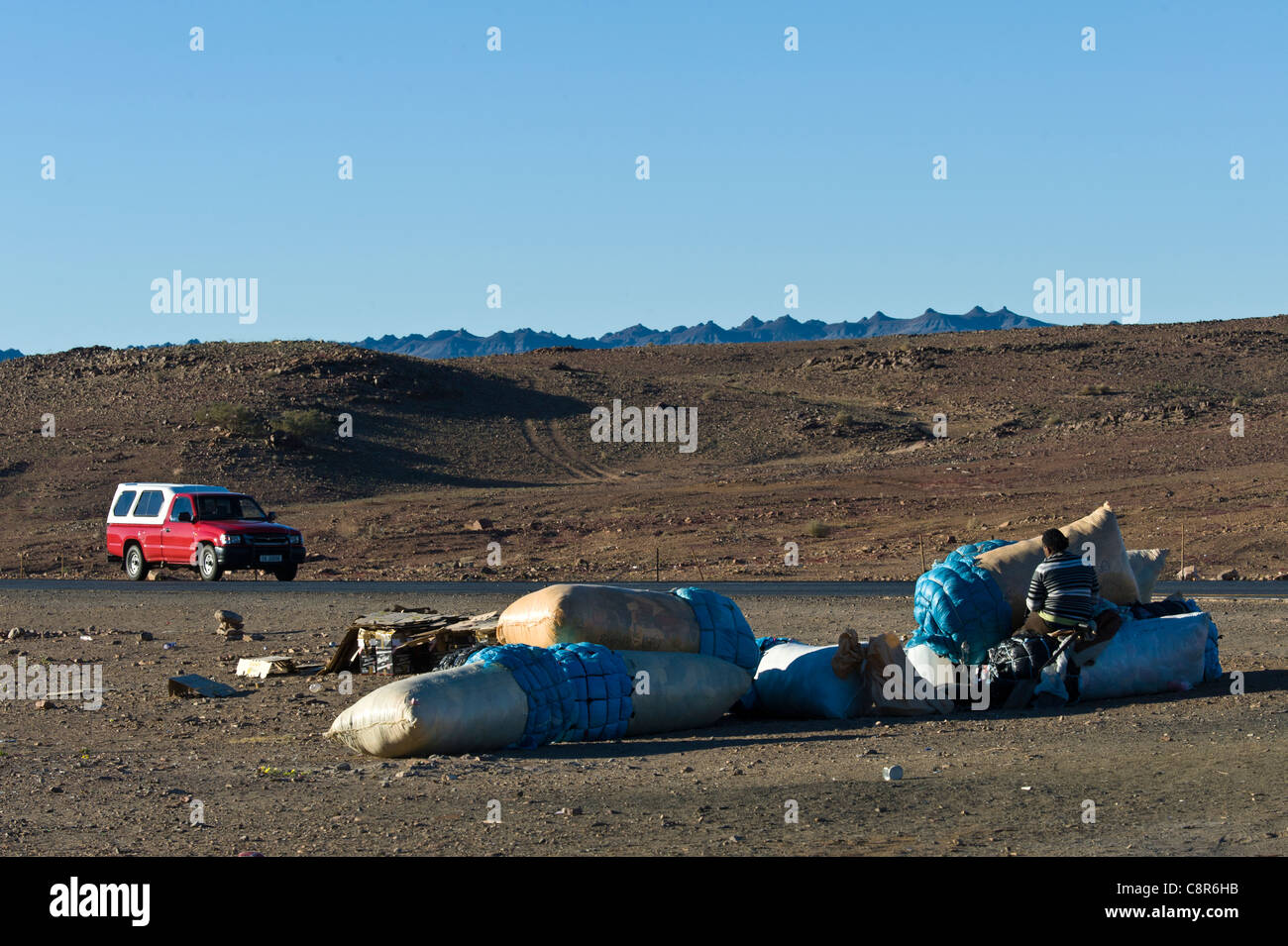Donna con sacchi di indumenti usati in attesa per il trasporto in Noordoewer Namibia Foto Stock