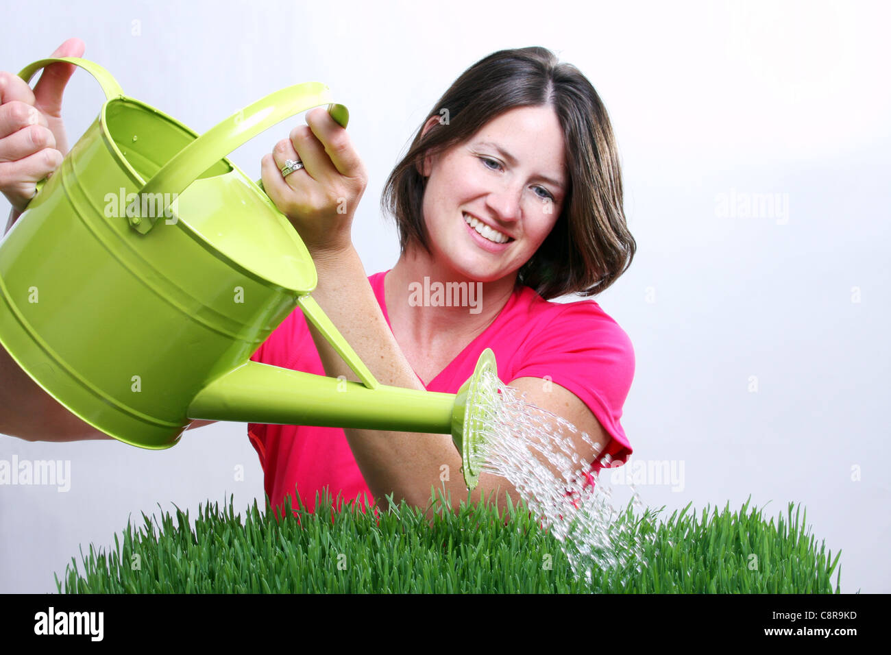 Una donna che guarda verso il basso mentre erba di irrigazione con una spolverata di concentrarsi sull'acqua Foto Stock