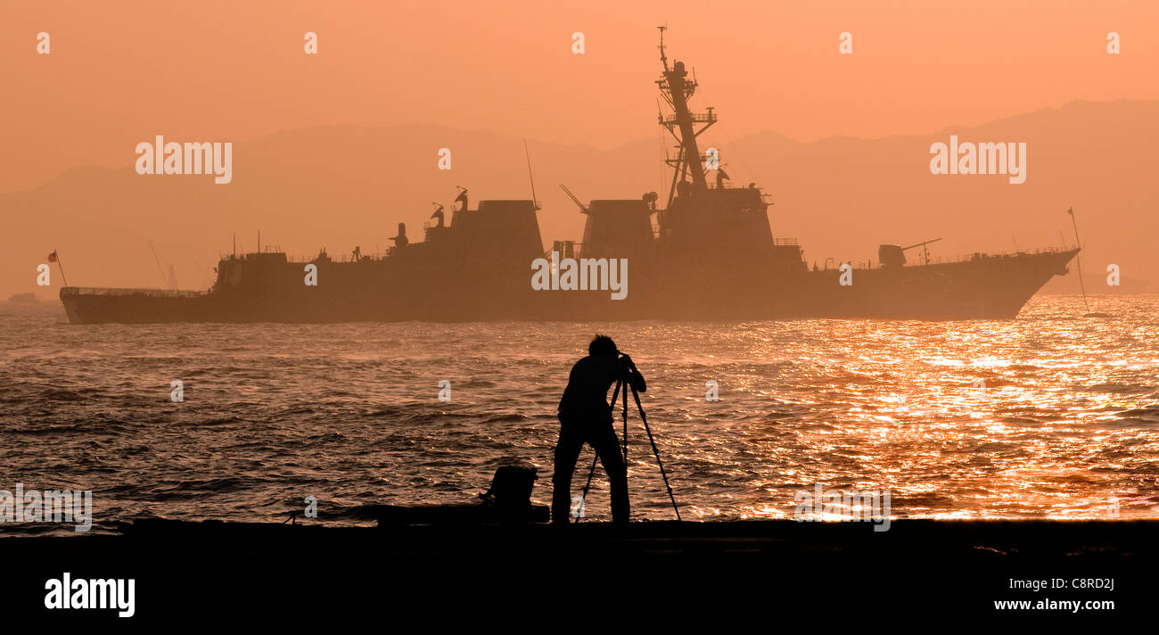 Un fotografo cinese di fotografare un USA navy battaglia navale stagliano al tramonto, Victoria Harbour, Hong Kong, Cina. Foto Stock