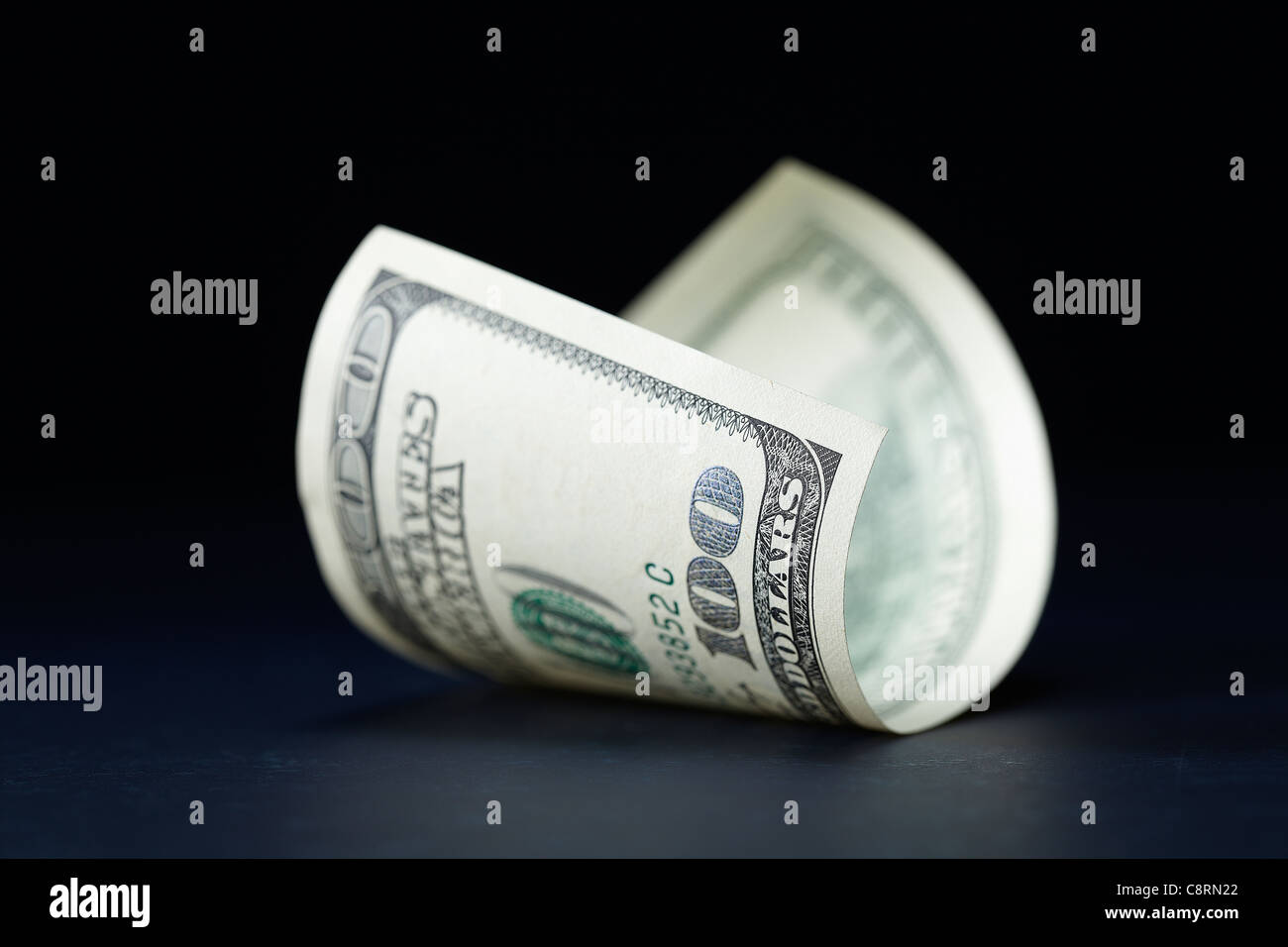 Piegato 100 dollar carta moneta contro uno sfondo scuro Foto Stock