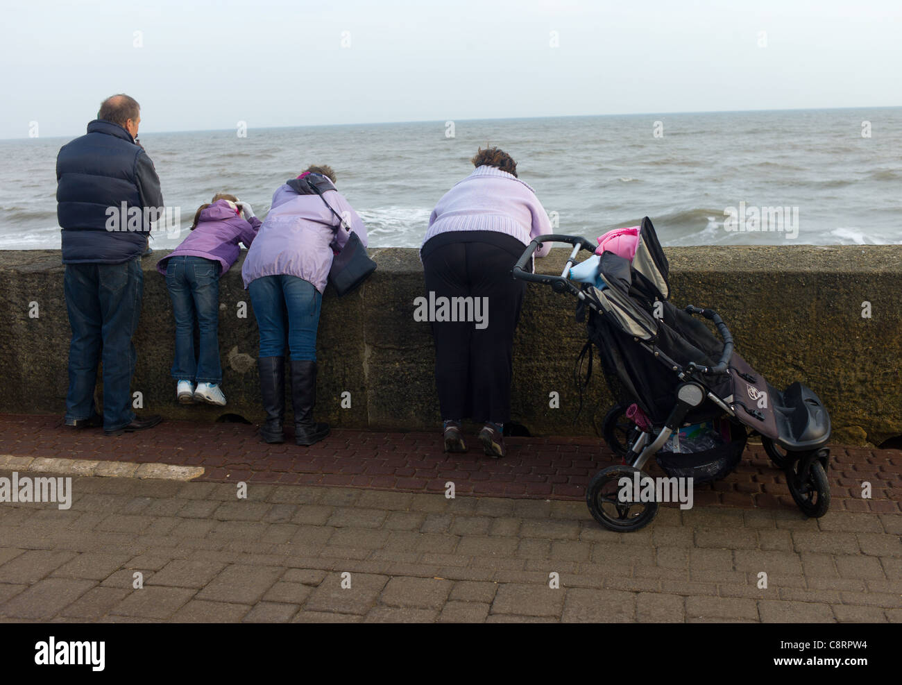 Famiglia vestito in giacche malva guardando le onde a Bridlington, Yorkshire, Regno Unito Foto Stock