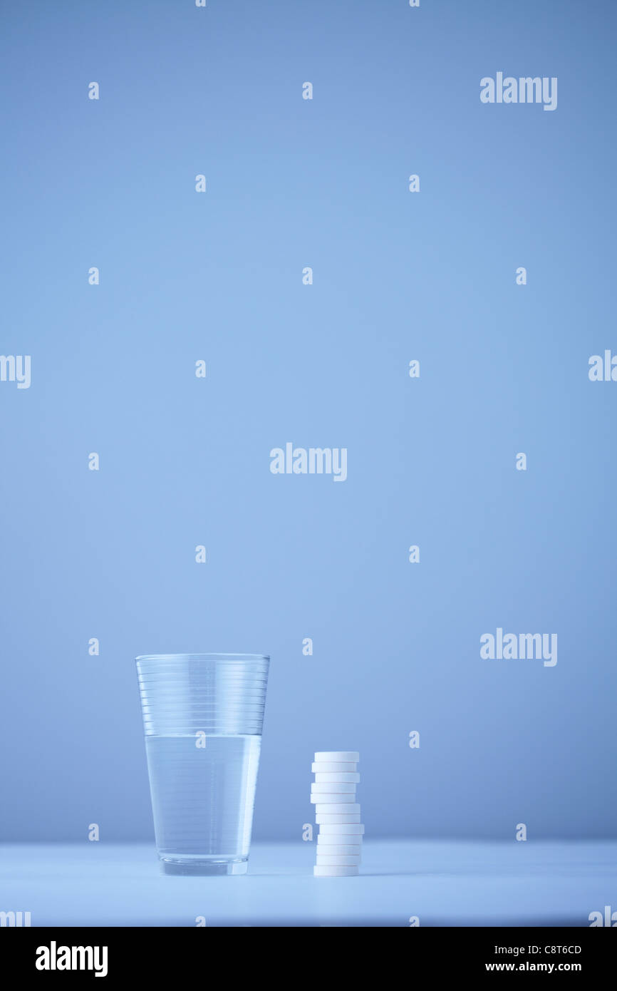 Pila di pillole lungo con un bicchiere di acqua sul bancone Foto Stock