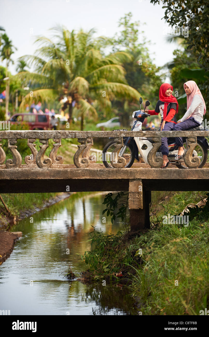 Due giovani ragazze malesi in sella a una motocicletta su un ponte. Foto Stock
