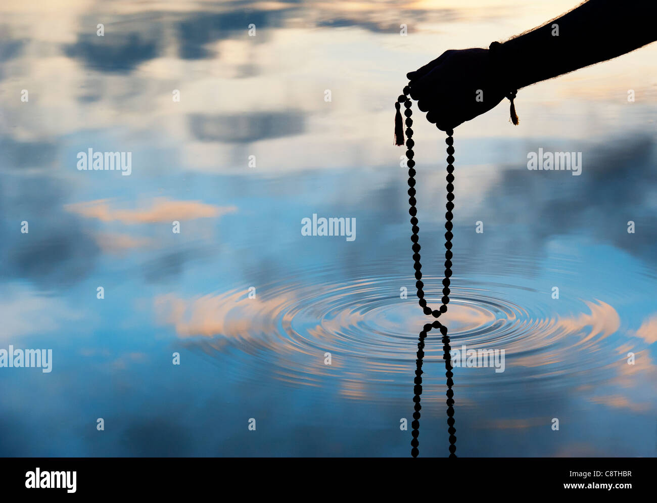 Mano azienda Rudraksha indiano / Japa Mala i grani di preghiera su acqua increspata . Silhouette Foto Stock
