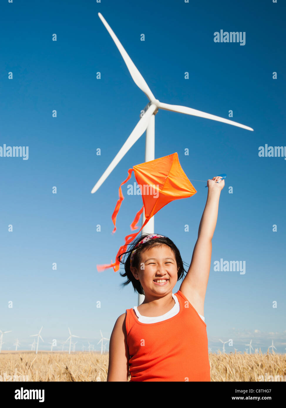 Stati Uniti d'America, Oregon, Wasco, ragazze 10-11) giocando con il kite in campo di grano, la turbina eolica in background Foto Stock
