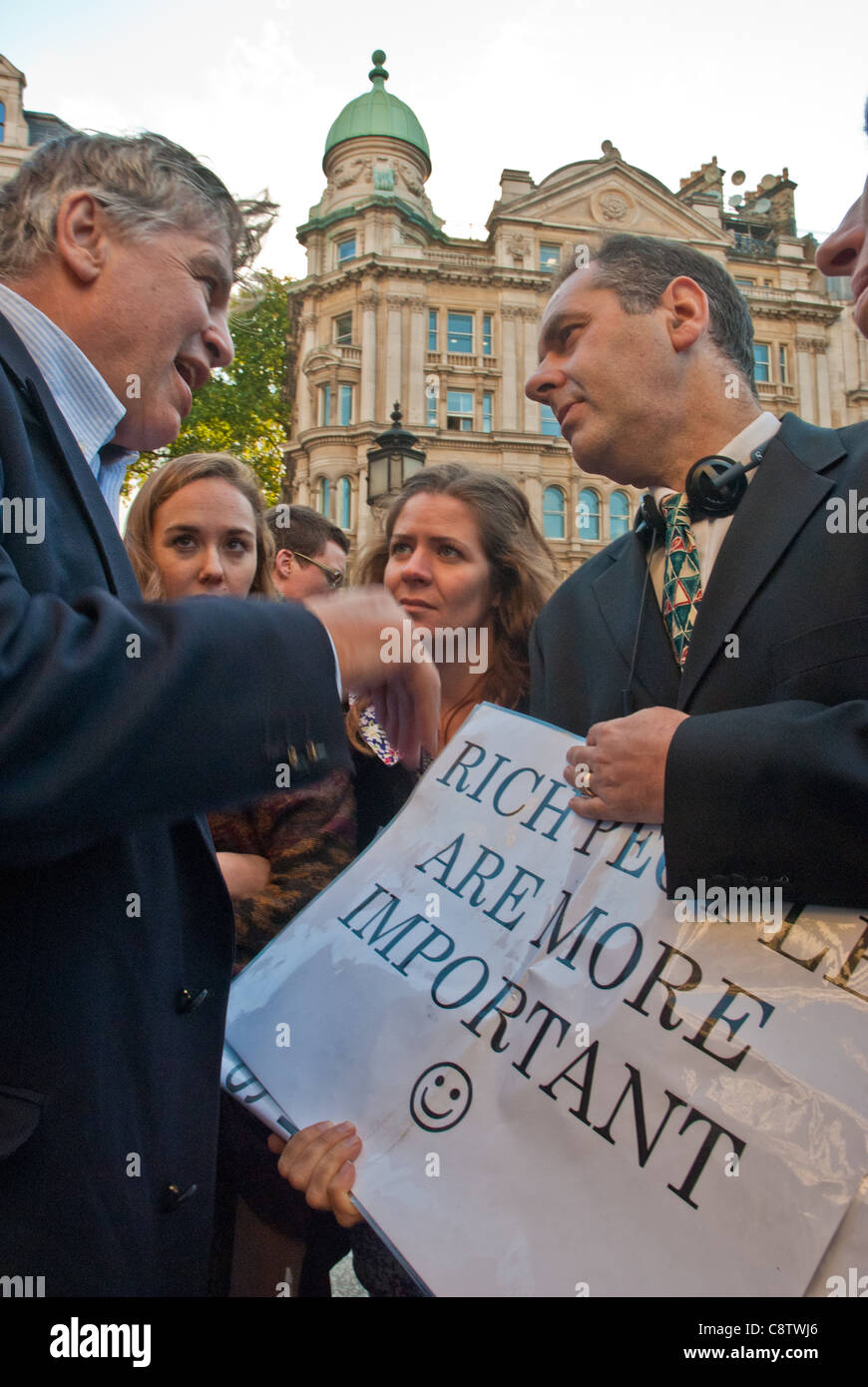 Occupare di Londra. Due uomini di mezza età in giacca (banchieri) hanno una seria discussione su un poster "ricchi sono più importante". Foto Stock