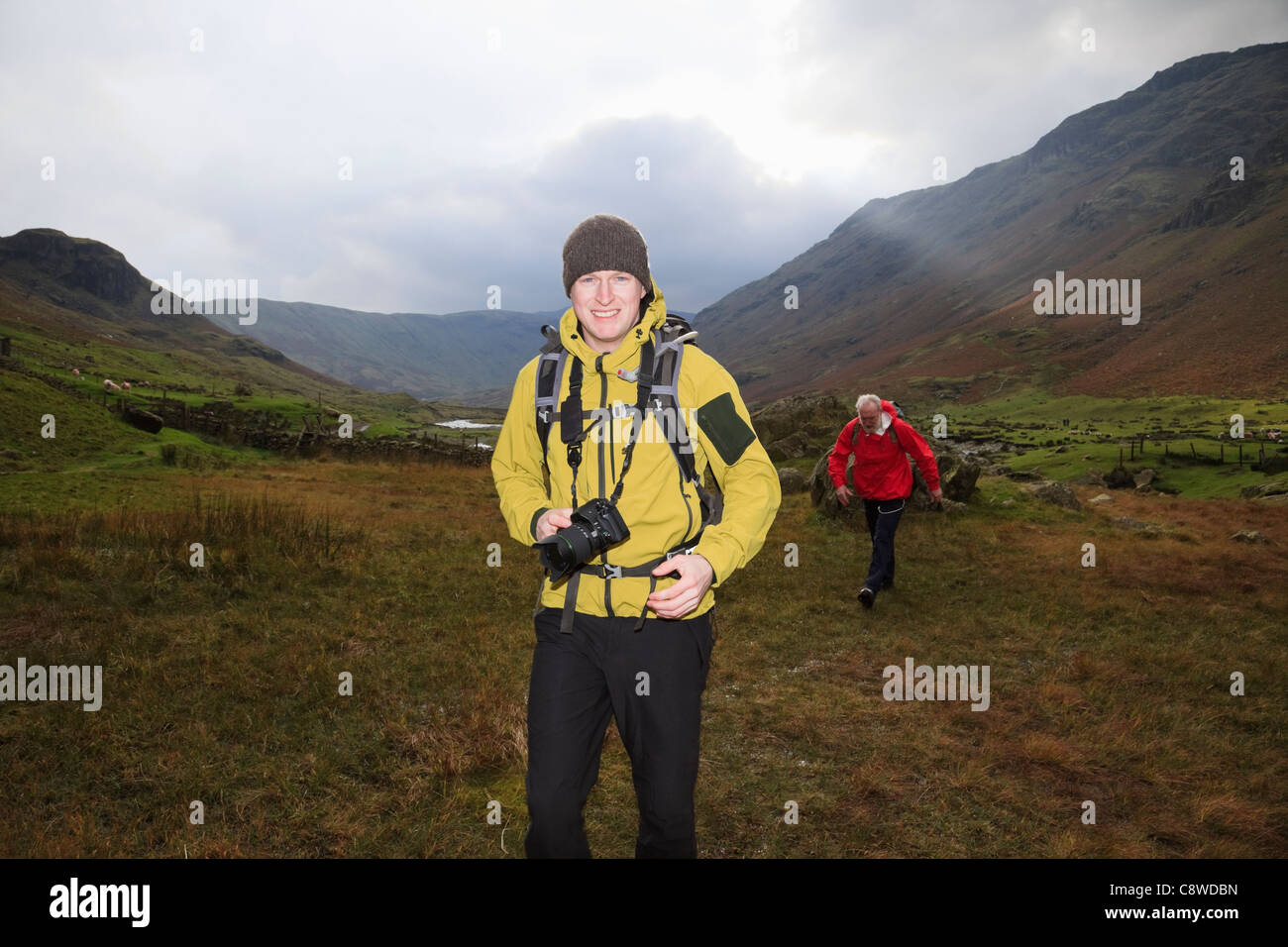 Uomo che porta una fotocamera reflex digitale a piedi nella valle Langstrath nel Parco Nazionale del Distretto dei Laghi Cumbria Inghilterra England Regno Unito Foto Stock