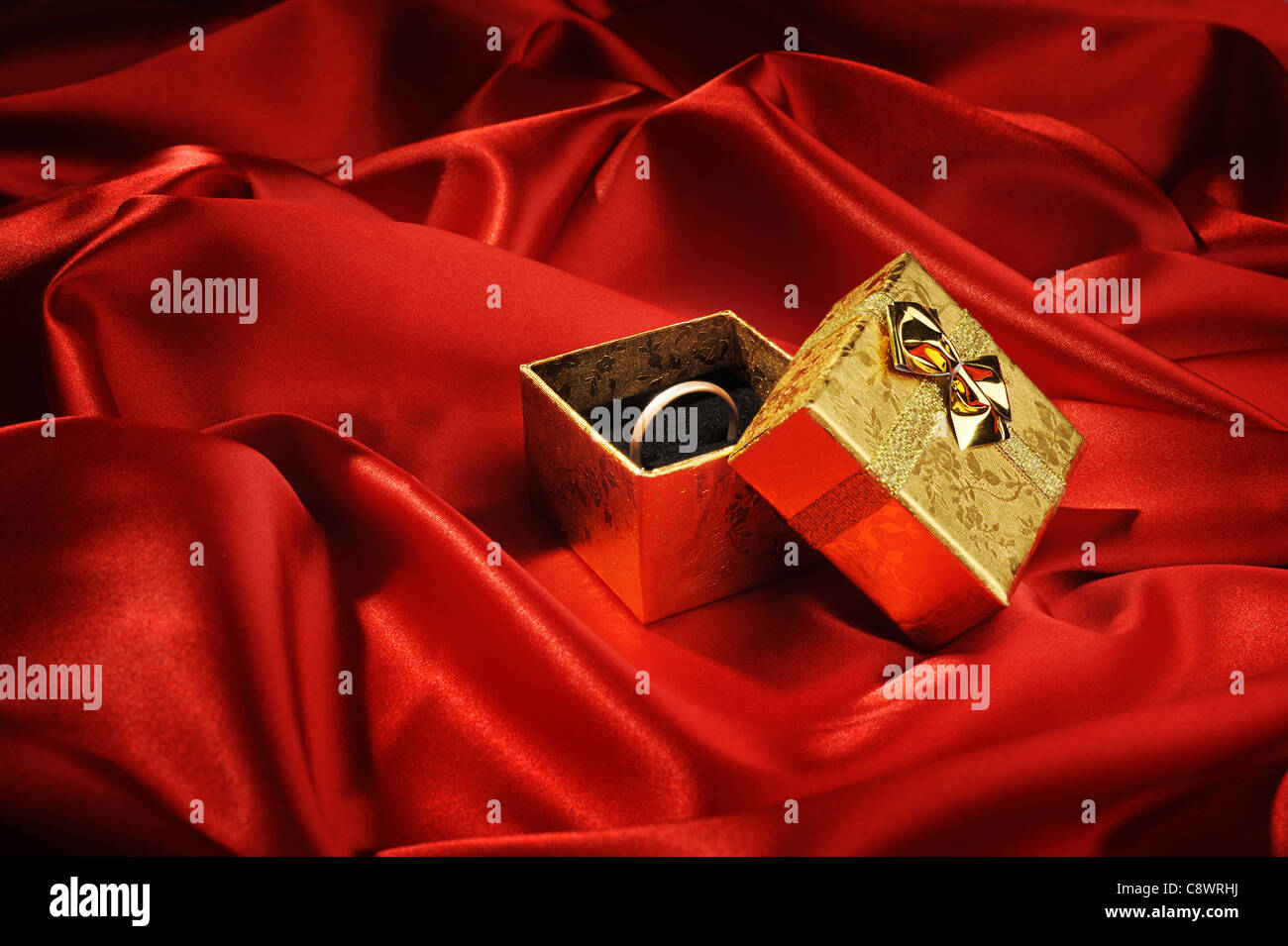 Scatole in oro con un anello di nozze su seta rossa Foto Stock