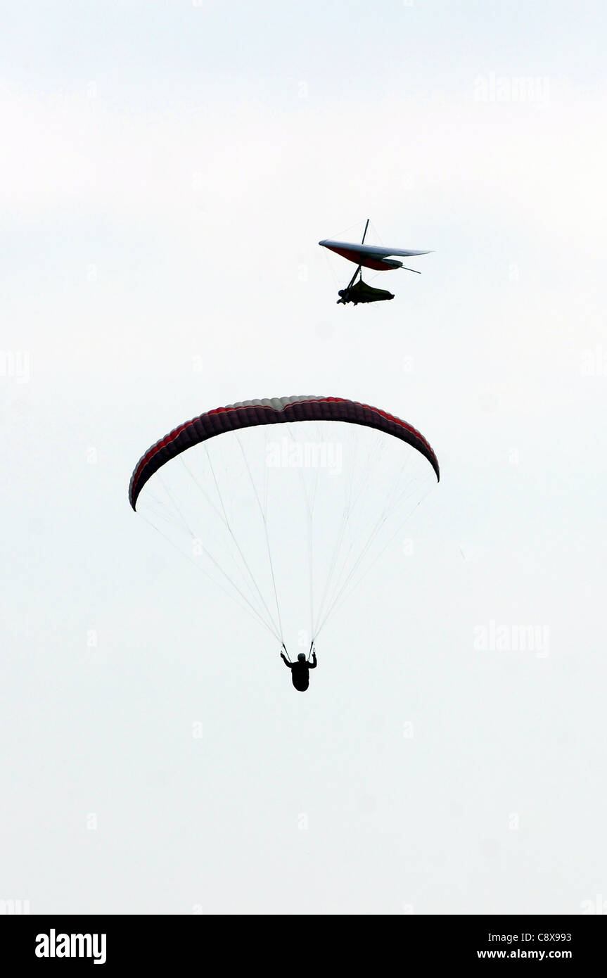 Un parapendio e deltaplano attraversare percorsi nel cielo sopra la baia di inizio in South Devon. Foto Stock