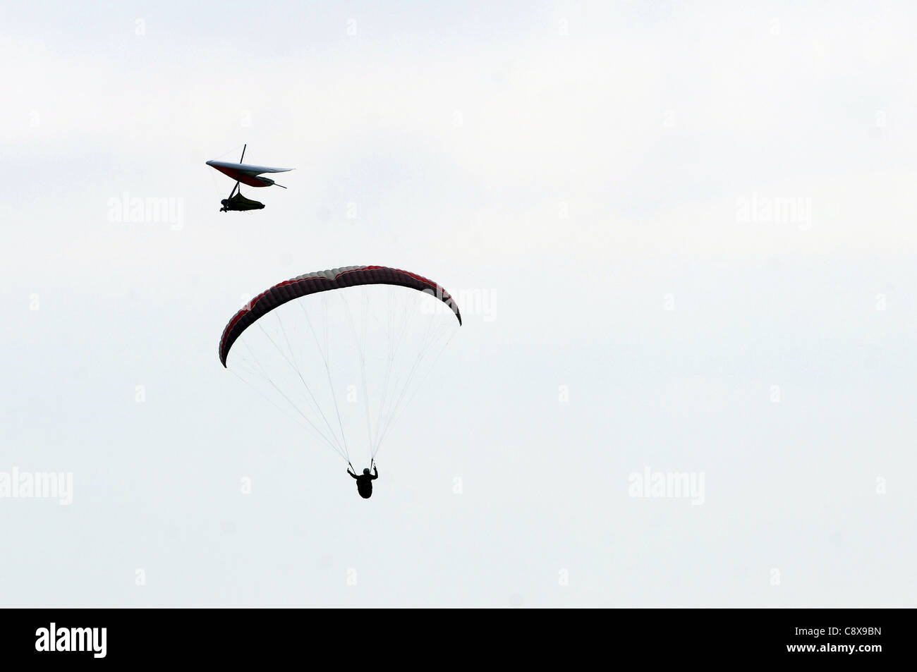 Un parapendio e deltaplano attraversare percorsi nel cielo sopra la baia di inizio in South Devon. Foto Stock