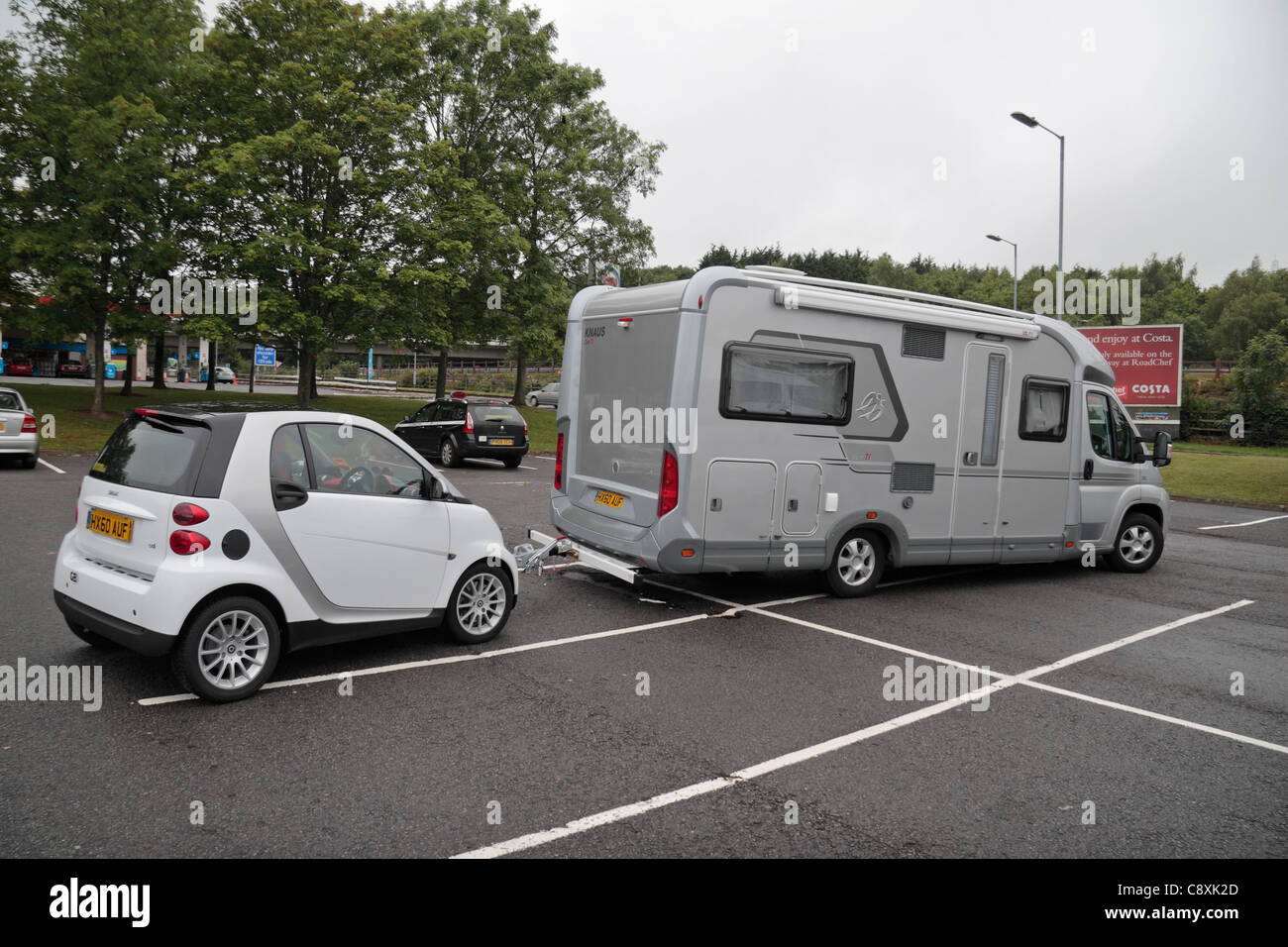 Autovettura di piccole dimensioni che viene trainato da un camper. Parcheggiate all' autostrada Rownhams Servizi sulla M27, Southampton, Hampshire, Regno Unito. Foto Stock