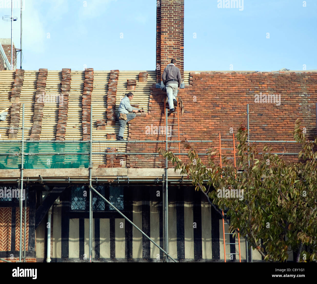 Gli uomini il rifacimento dei tetti edificio storico con mattonelle di terracotta, Thorpeness, Suffolk, Inghilterra Foto Stock
