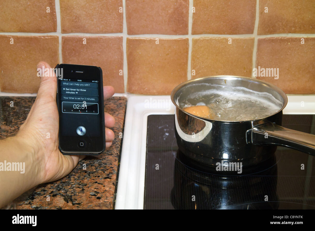 Utilizzando Siri personal assistant applicazione su un iPhone 4S utilizzando Controllo vocale per impostare il timer per tre minuti mentre le uova di ebollizione Foto Stock
