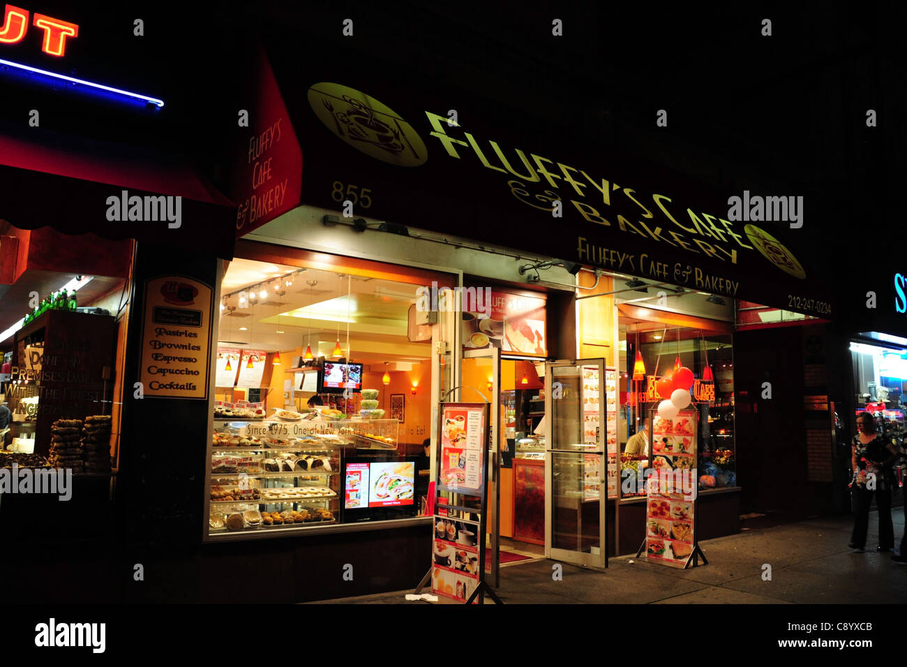 Night Shot vista sul marciapiede Fluffy's Cafe, luci elettriche illuminato ripiani alimentare le finestre di vetro porta aperta, 7th Avenue, New York Foto Stock