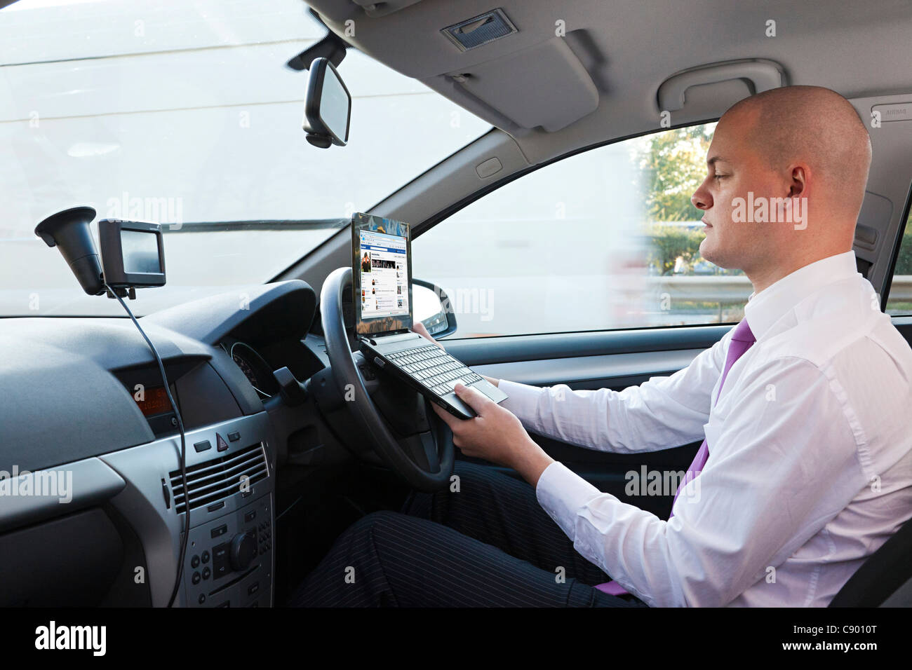 Uomo che utilizza il computer portatile durante la guida di auto in autostrada Foto Stock