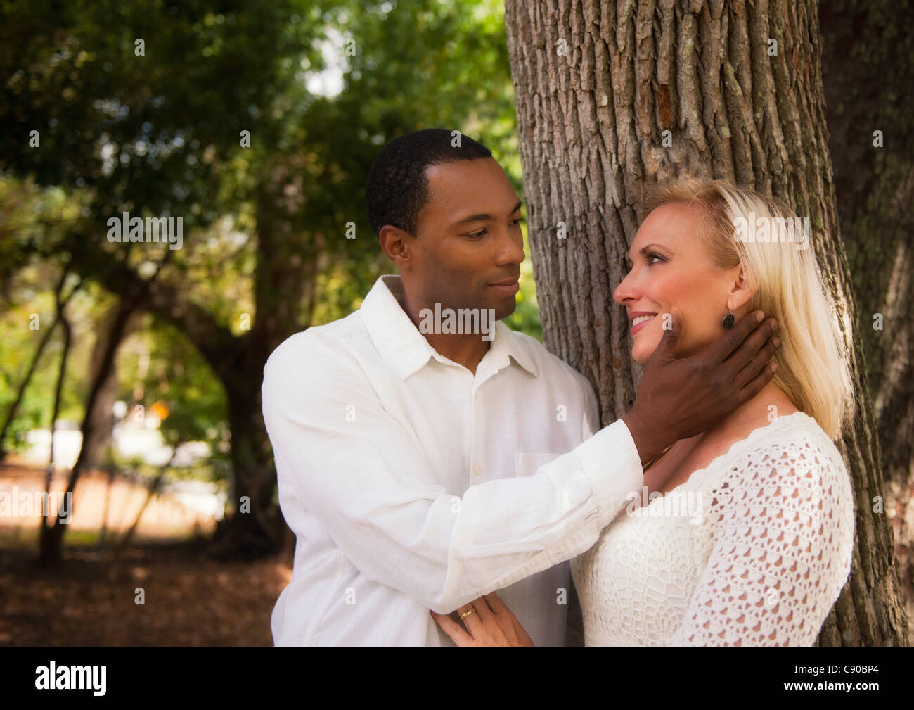 Afro-americano di maschio e femmina bianca intima momento al parco. Egli è in possesso la sua faccia teneramente con una sola mano. Foto Stock