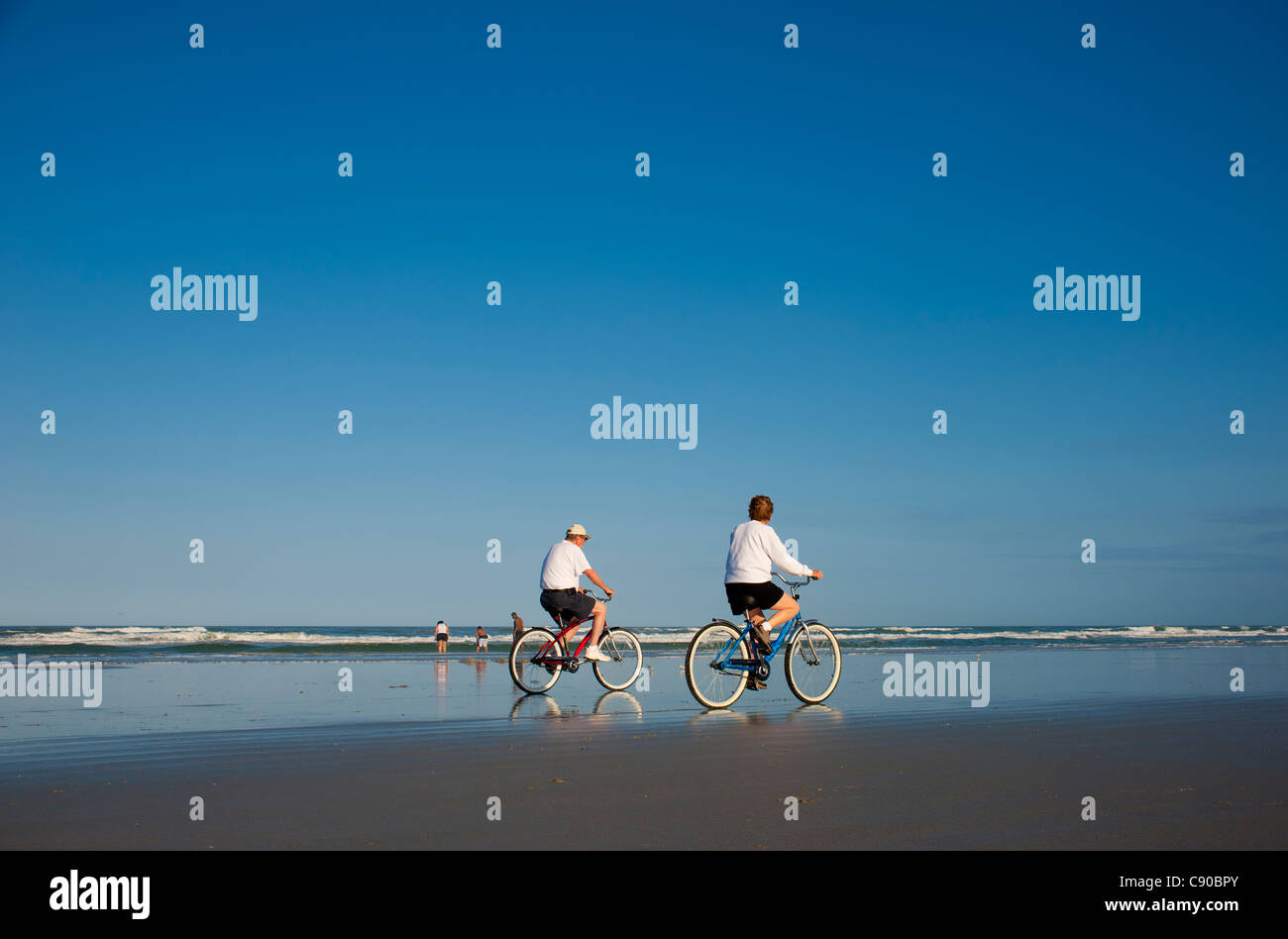 Coppia senior guidare la bicicletta bici sulla spiaggia accanto al mare nel tardo pomeriggio visto da dietro Foto Stock