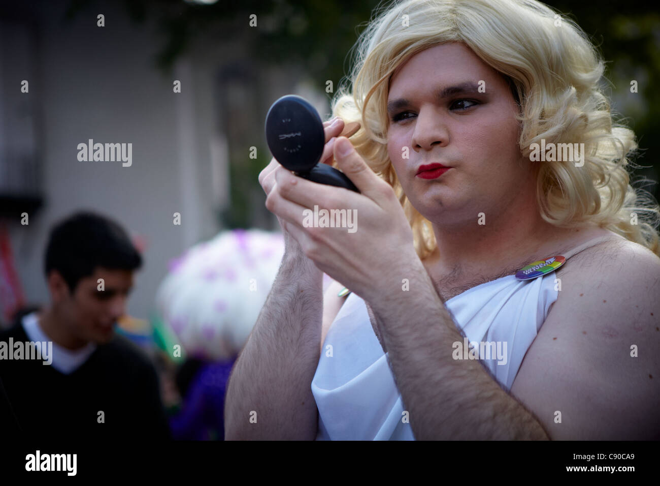 uomo gay nella marcia del gay pride. Ragazza transgender in abito bianco che applica il trucco, guardando nello specchio portatile, LGBT Rights march Foto Stock