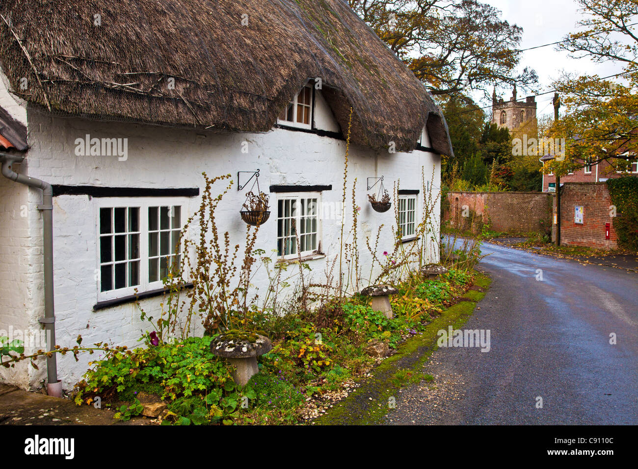 Tipico English Country Village road con un cottage con tetto di paglia e chiesa in distanza. Clyffe Pypard, Wiltshire, Inghilterra, Regno Unito Foto Stock