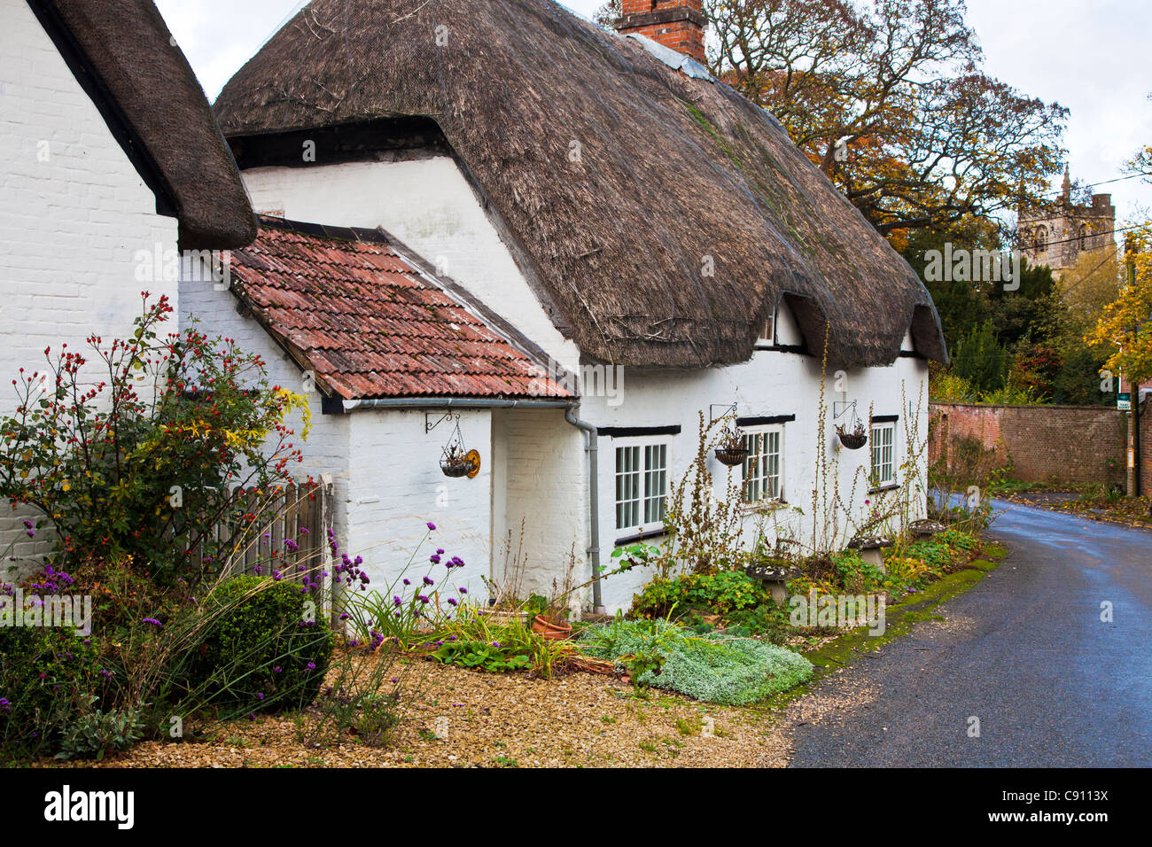 Tipico English Country Village road con un cottage con tetto di paglia e chiesa in distanza. Clyffe Pypard, Wiltshire, Inghilterra, Regno Unito Foto Stock