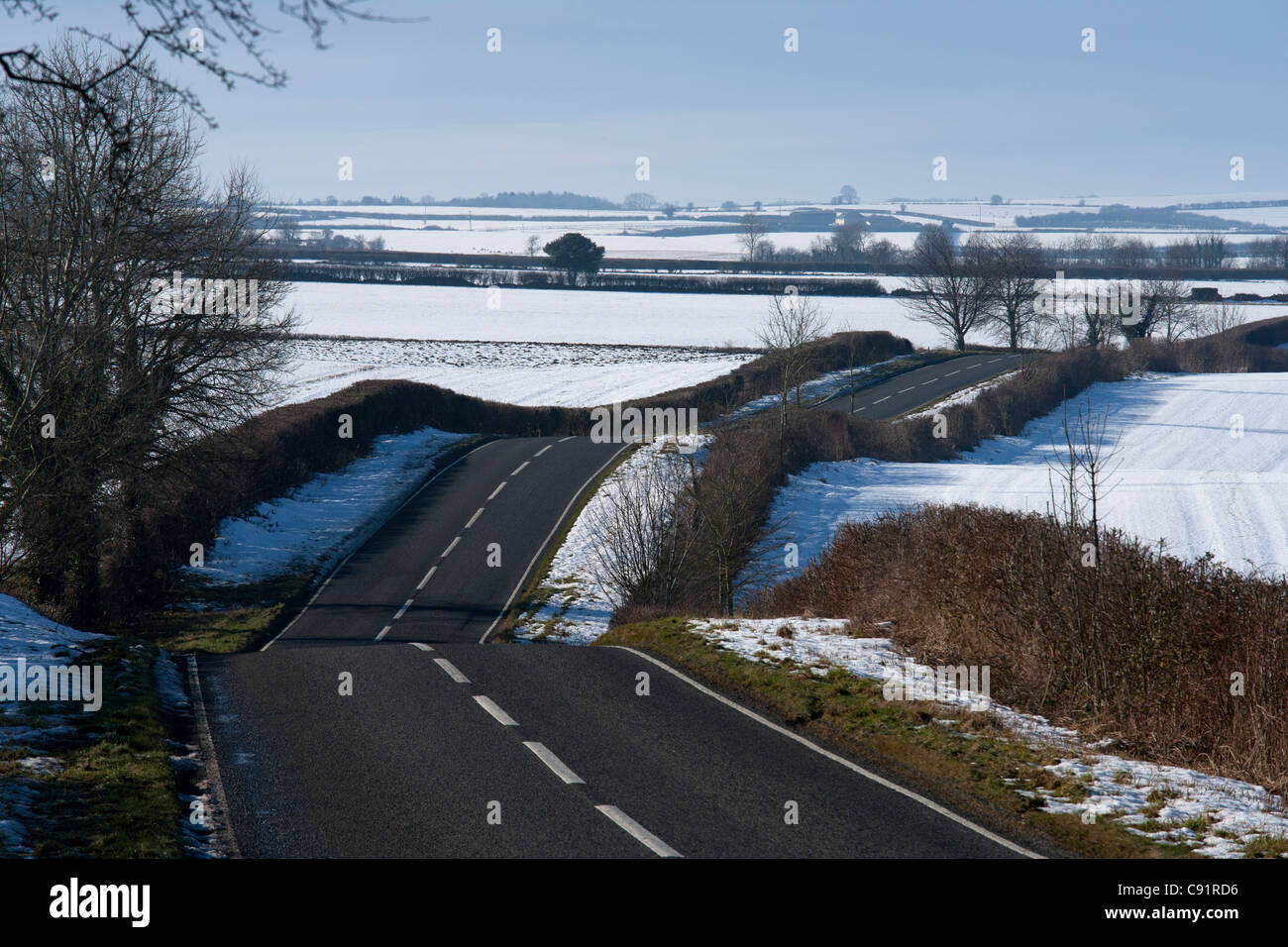 Windy strada accidentata taglio attraverso i campi di neve della campagna in inverno, Inghilterra Foto Stock