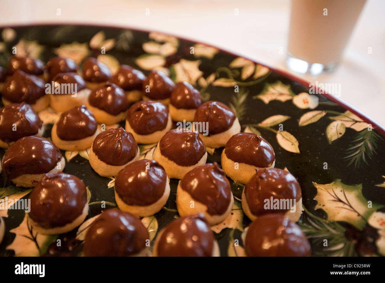 Primo piano di un raffinato nero e oro vassoio di ciliegia-riempito i cookie, mano-immersi nel cioccolato per Natale con un bicchiere di latte Foto Stock