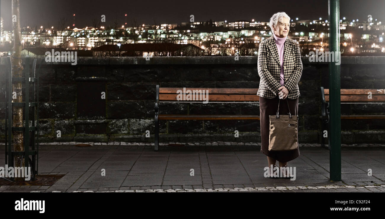 Donna anziana in attesa per il bus di notte Foto Stock