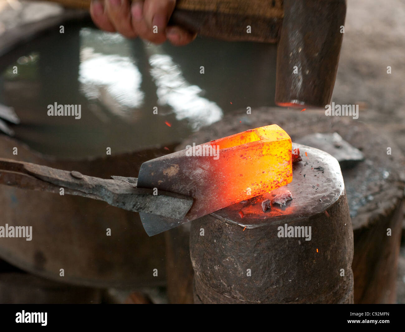 Fabbro utilizzando un martello pesante per forgiare una ax Foto Stock