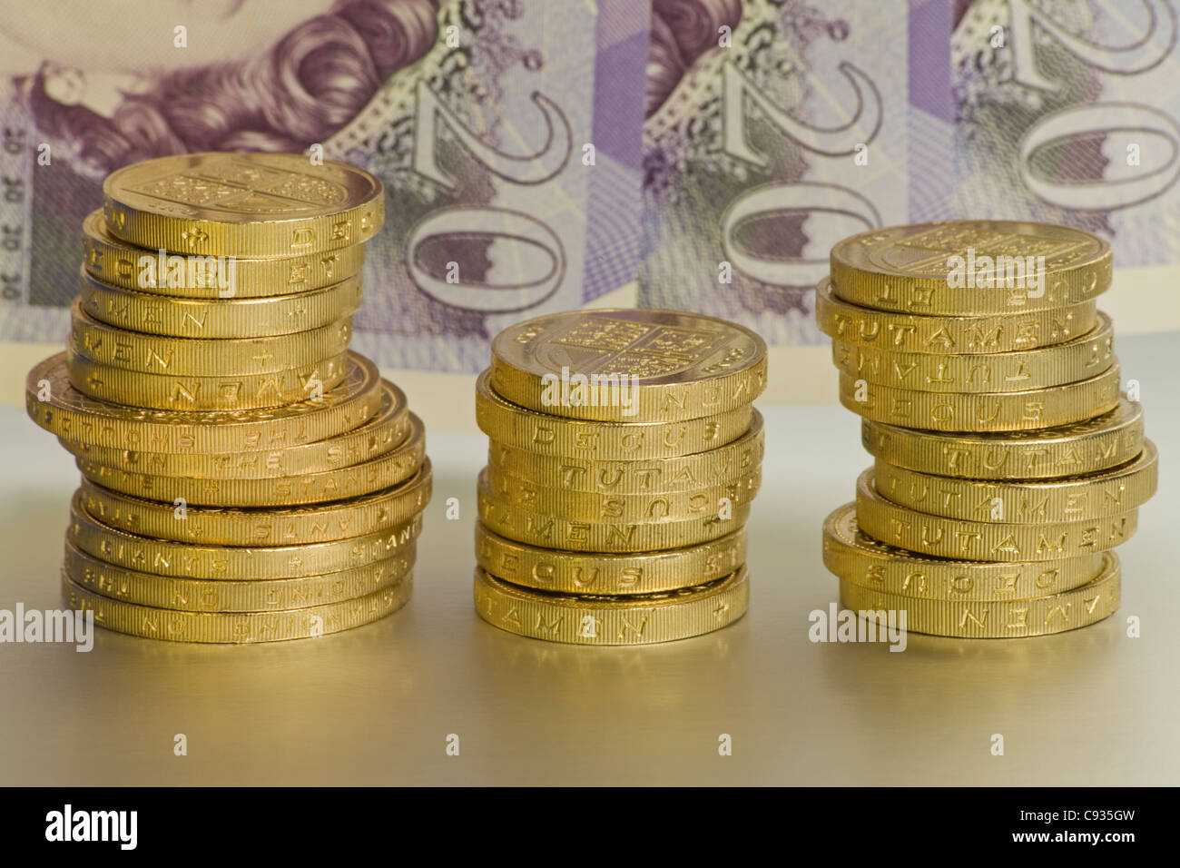 Uno e due libbre di monete in tre pile di fronte tre venti pound note Foto Stock