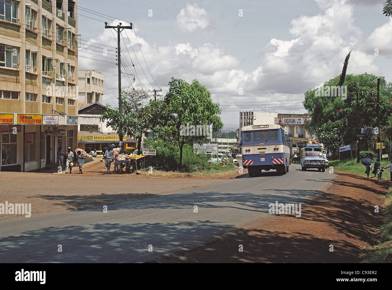 Bus sulla strada principale attraverso Embu città del Kenya con edificio moderno negozi auto palo del telegrafo e asfalto stradale sigillato e matatu taxi Foto Stock