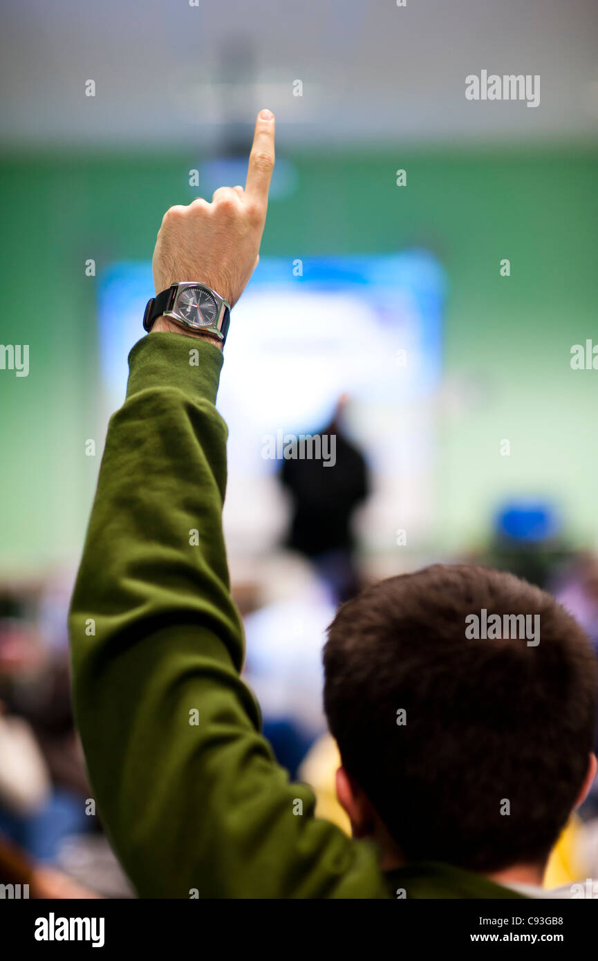 Vista posteriore di un giovane uomo tenendo la sua mano fino a fare una domanda in una riunione, REGNO UNITO Foto Stock