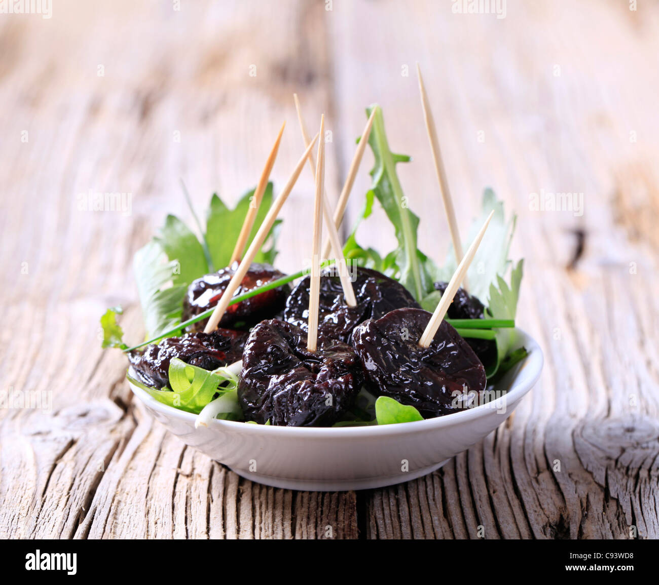 Le prugne secche vetrata su un nido di insalata verde Foto Stock