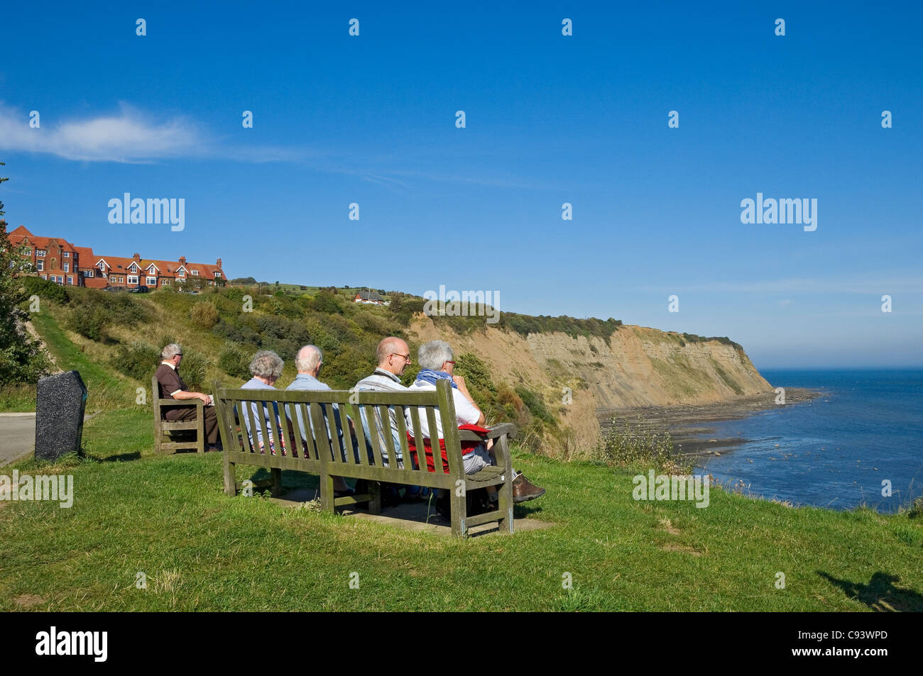 I turisti anziani che si trovano seduti sulla panca che guarda fuori Mare in estate Robin Hoods Bay North Yorkshire Inghilterra Regno Unito Gran Bretagna Foto Stock